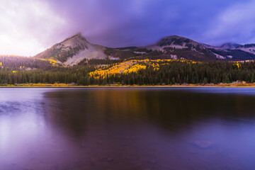 Epic purple Sunrise over Lost Lake Colorado smooth water in Autumn with yellow Aspen trees and snow covered mountains. 