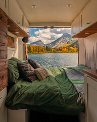 Campervan Vanlife Bed in Wilderness Colorado Mountain Aspen Tree Lake in Autumn Fall Foliage. Green Bedding and Wooden Details with Back Door Open.