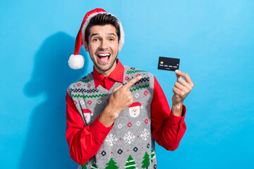 Photo portrait of handsome young guy hold point credit card wear x-mas print vest hat outfit isolated on blue color background - obrazy, fototapety, plakaty