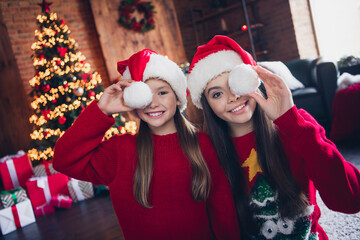 Photo of cheerful tricky little siblings dressed ugly print christmas jumpers cap baubon cover eyes...