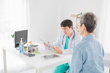 asian doctor talk with old patient in hospital, he screening and write patient information on patient chart, elderly healthcare promotion