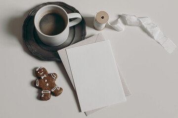Christmas stationery. Blank greeting card, invitation mockup. Gingerbread man cookies, cup of coffee. Vintage silver plate. Neutral white table background, ribbon. Winter breakfast still life, flatlay