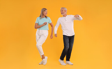 Senior couple dancing together on orange background - obrazy, fototapety, plakaty