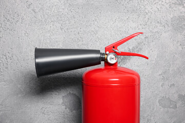 Red fire extinguisher near grey wall, closeup