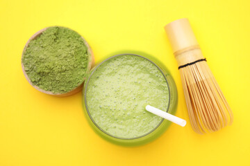 Glass of tasty matcha smoothie, powder and bamboo whisk on yellow background, flat lay