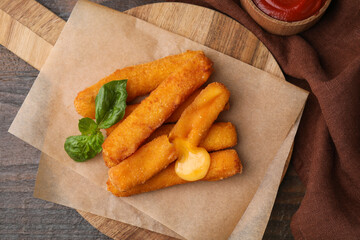 Tasty fried mozzarella sticks and basil on wooden table, flat lay