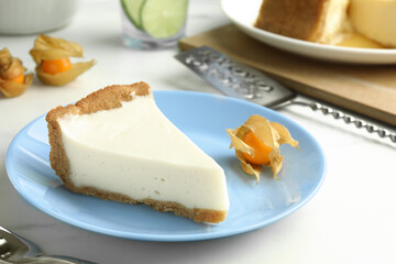 Piece of tasty vegan tofu cheesecake and physalis fruit on white table, closeup