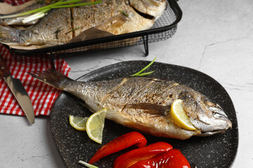 Delicious baked fish served with bell pepper and lemon on light textured table. Seafood