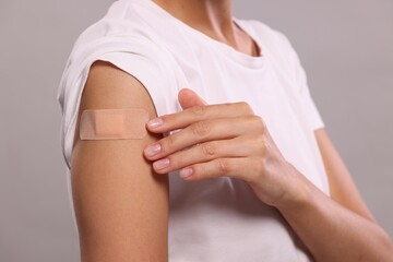 Woman with sticking plaster on arm after vaccination against light grey background, closeup