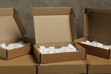 Many closed and open cardboard boxes with pieces of polystyrene foam on grey textured background