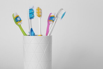 Different toothbrushes in holder on light grey background, closeup. Space for text