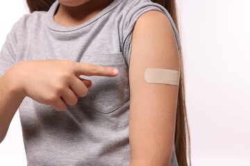 Girl pointing at sticking plaster after vaccination on her arm against white background, closeup