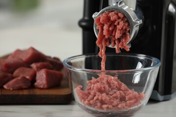 Electric meat grinder with beef mince on white table against blurred background, selective focus. Space for text