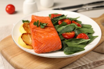 Tasty grilled salmon with basil, tomatoes and lemon on table, closeup