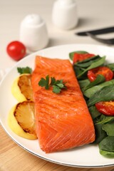 Tasty grilled salmon with basil, tomatoes and lemon on table, closeup