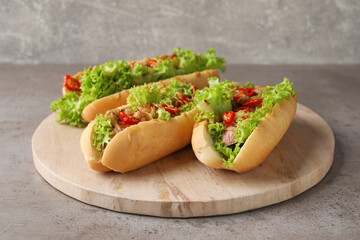 Tasty hot dogs with chili, lettuce and sauce on grey textured table, closeup