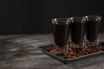 Shot glasses with coffee liqueur and beans on grey textured table, space for text