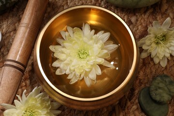 Tibetan singing bowl with water, beautiful chrysanthemum flowers, mallet and stones on table, flat...