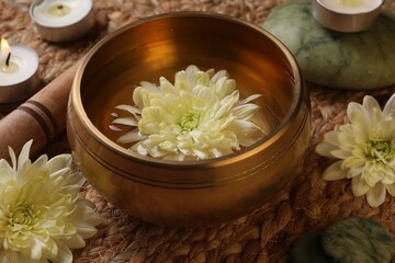 Obraz na płótnie Canvas Tibetan singing bowl with water, beautiful chrysanthemum flowers, mallet and burning candle on table, closeup