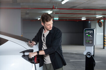 Young man travel with EV electric car to shopping center parking lot charging in downtown city...