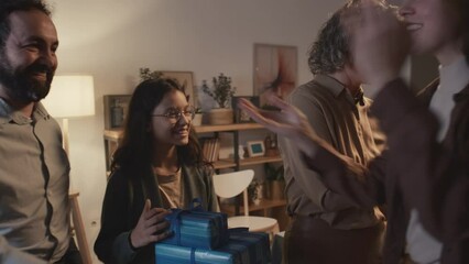 Medium shot of cheerful young Jewish husband in yarmulke and wife arriving at Hanukkah party at friends house, greeting each other, hugging, chatting and exchanging gifts