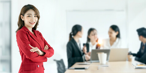 Portrait of beautiful business woman standing with arms crossed in front of business team, looking at camera.