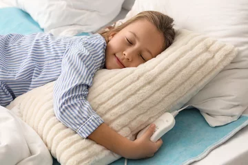 Tuinposter Little girl sleeping on electric heating pad in bedroom © Pixel-Shot