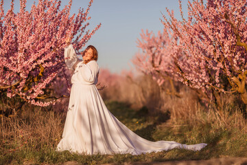 Woman blooming peach orchard. Against the backdrop of a picturesque peach orchard, a woman in a...
