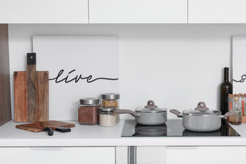 White kitchen counter with electric stove, cooking pots and utensils