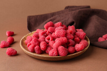 Plate with fresh raspberries on brown background