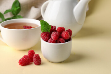Bowl with fresh raspberries and cup of tea on yellow table