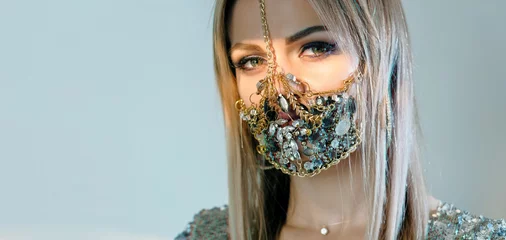 Foto op Plexiglas Pandemic fashion. Quarantine DIY accessories. Portrait of sensual woman in glamour handmade chain gemstone face mask posing isolated on blue copy space background. © golubovy