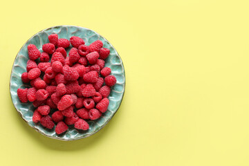 Plate with fresh raspberries on yellow background