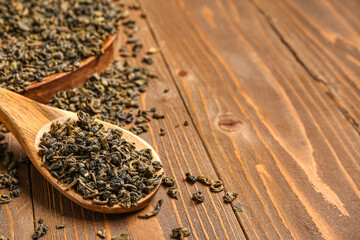Spoon and tray with green tea leaves on wooden background