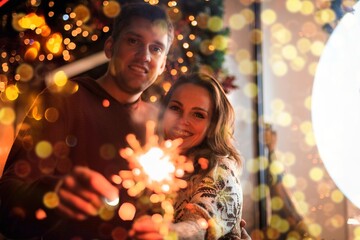 Obraz na płótnie Canvas Beautiful couple holding sparklers celebrating christmas. Happy holiday