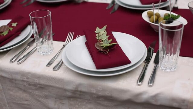 Elegant table setting at festive event with red napkins, white plates, ivy decoration, sophisticated dining setup for wedding or gala banquet, trend in holiday event design.
