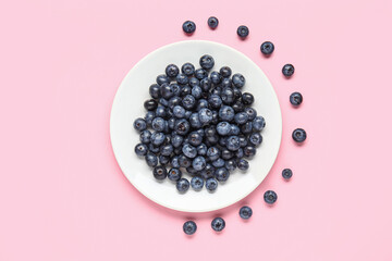 Plate with fresh blueberries on pink background