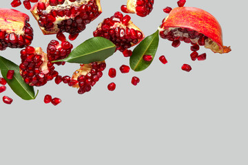 Flying fresh pomegranates with seeds and leaves on grey background