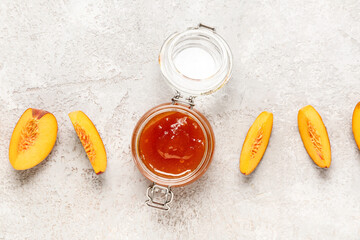 Slices of ripe peach and jar with tasty jam on grunge background