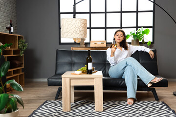 Young woman with glass of wine sitting on couch at home
