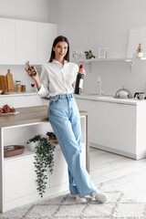 Young woman with opener and bottle of wine in kitchen