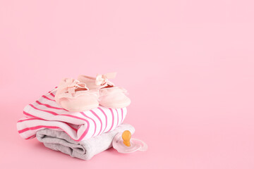 Stylish baby shoes with clothes and pacifier on pink background