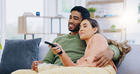 Couple, watching tv and popcorn on living room sofa for smile, hug or relax with remote for choice,...