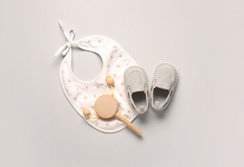 Stylish baby shoes with bib and rattle on grey background