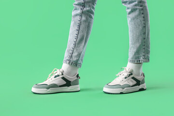 Legs of young woman in stylish sneakers on green background