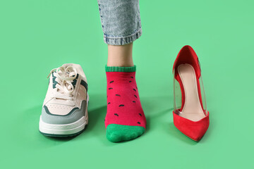 Leg of young woman with red high heel and stylish sneaker on green background