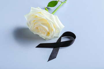 Beautiful rose flower and black funeral ribbon on grey background