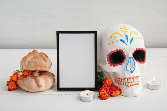 Bread of the dead with flowers, candles, frame and painted skull on white wooden table. Celebration of Mexico's Day of the Dead (El Dia de Muertos)