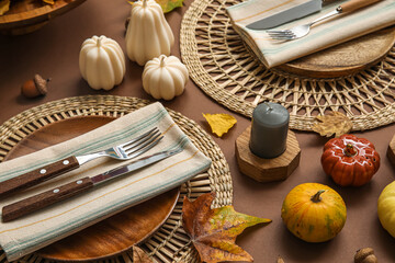 Stylish table setting with candles and autumn decor on brown background