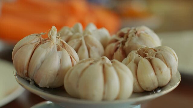 Garlic lies on a plate. Large juicy garlic in the skin is ready as an ingredient for Uzbek pilaf. The smell of garlic wafts through the room. The garlic heads are ready for cooking